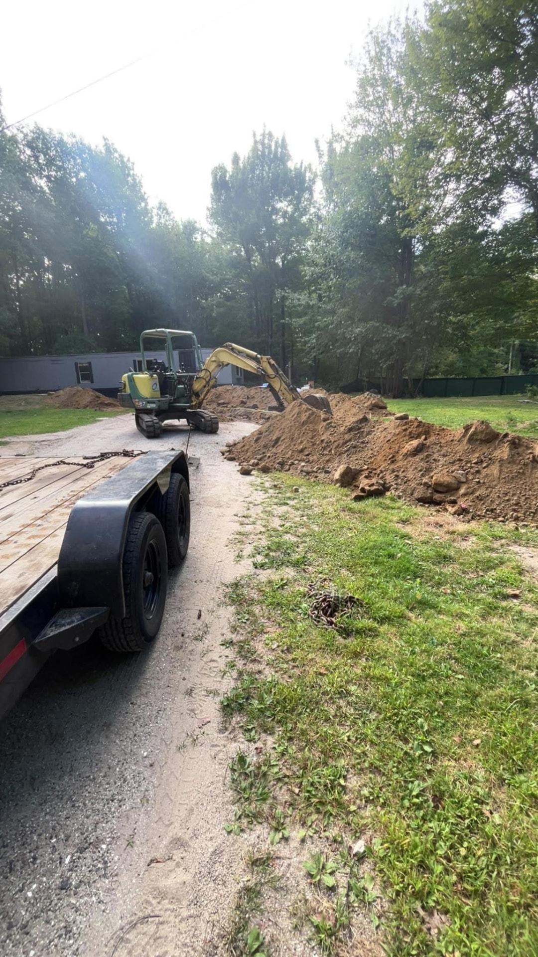 Mini excavator digging a trench along a gravel driveway