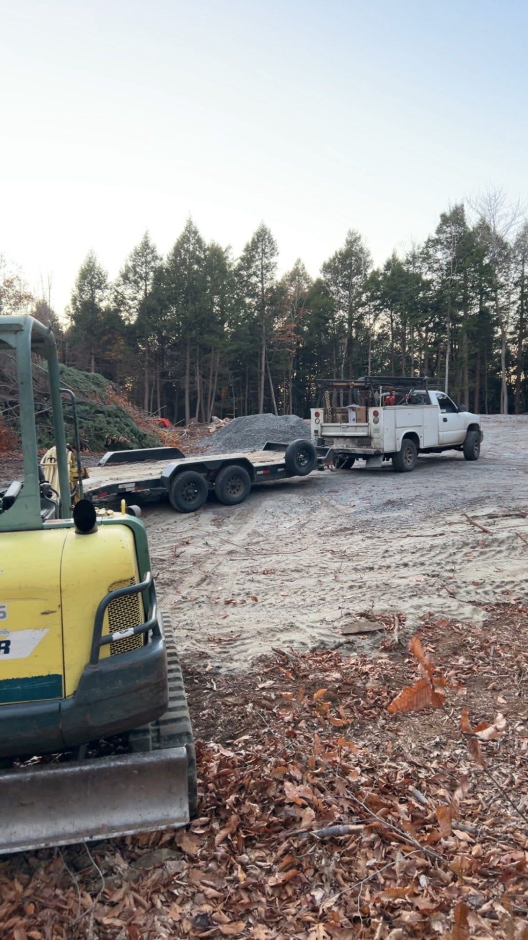Cleared and graded lot with excavator, trailer, and work truck on site