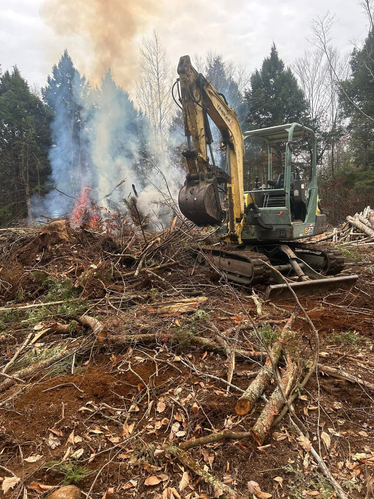Excavator feeding a brush pile burn during a land clearing job